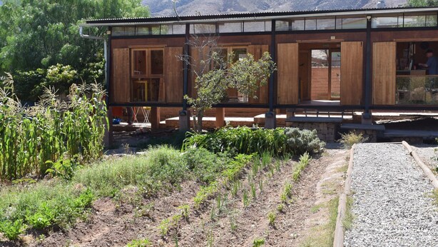 A wooden building with a glass facade, surrounded by a gravel path and vegetation, with mountains in the background. - Glamping Tilcara El Obrador (Tilcara)
