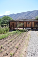 Un edificio de madera con fachada de vidrio, rodeado por un camino de grava y vegetación, con montañas al fondo.