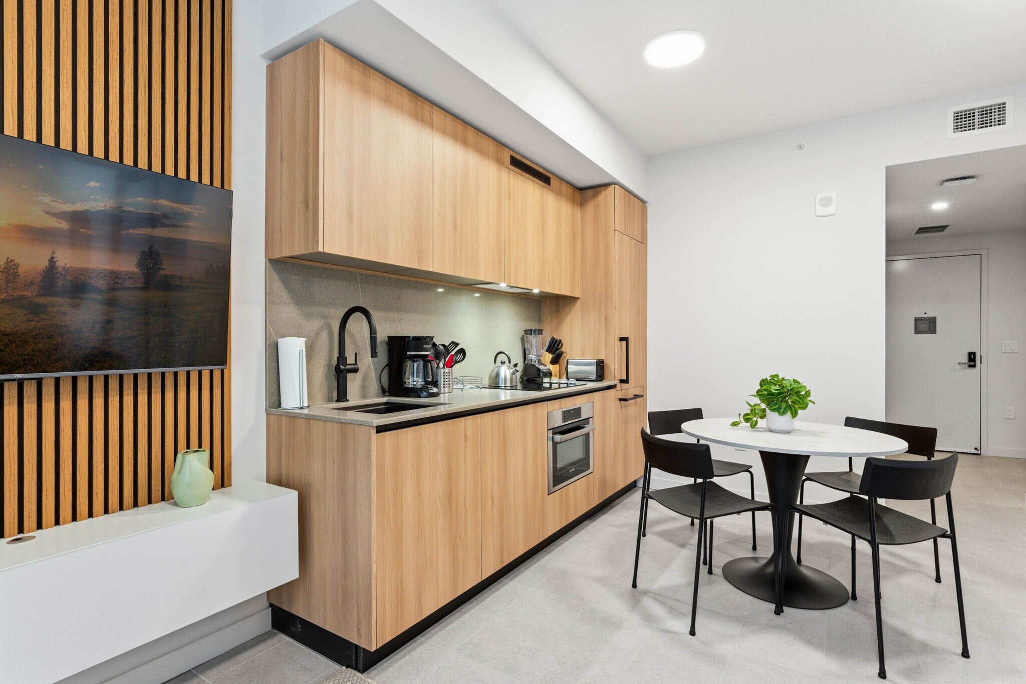 A modern kitchen with wooden cabinets, a built-in oven, a sink, and a dining area with a round table and chairs.