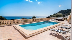 Una piscina con sillones de descanso, vista al mar y un paisaje montañoso.