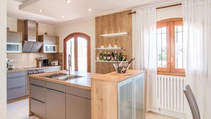 Una cocina moderna con una isla central, electrodomésticos integrados y un ventanal con cortinas.