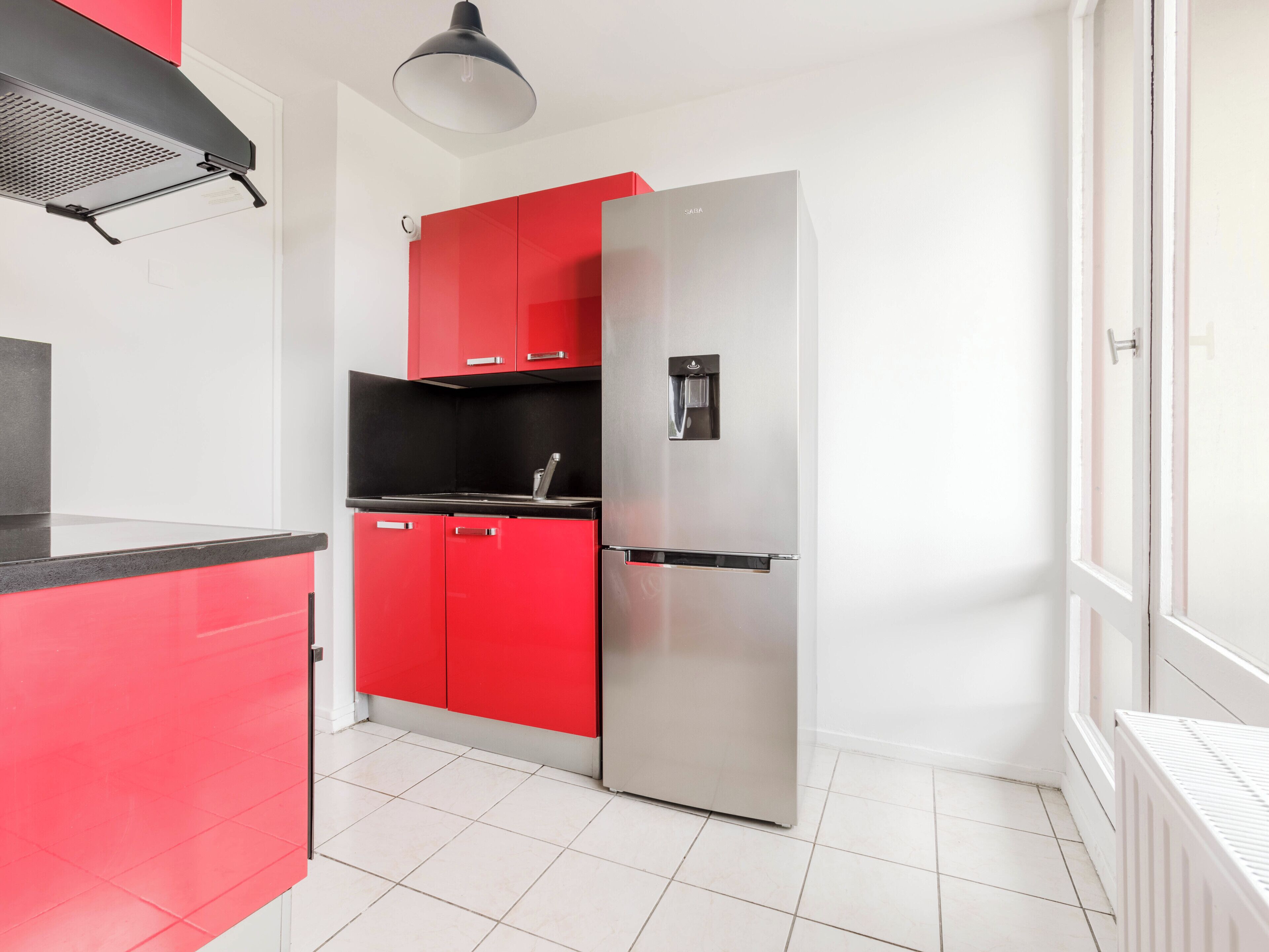 A compact kitchen with a stainless steel refrigerator, red cabinets, and a black countertop.