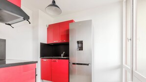Una cocina compacta con un refrigerador de acero inoxidable, gabinetes rojos y una encimera negra.