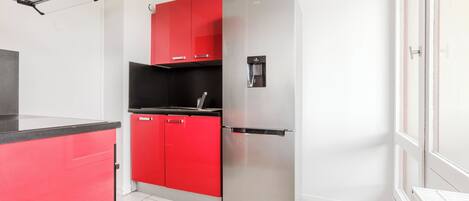 A compact kitchen with a stainless steel refrigerator, red cabinets, and a black countertop.