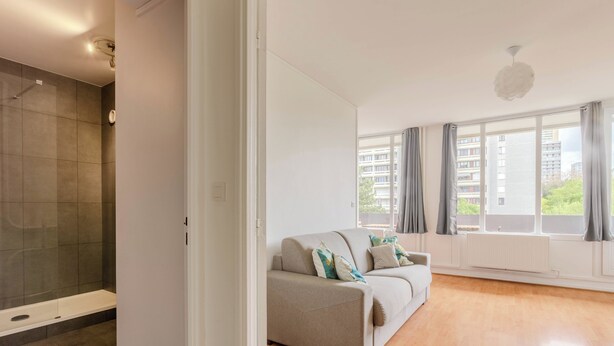 Un apartamento moderno con ducha, sofá y ventanas amplias.