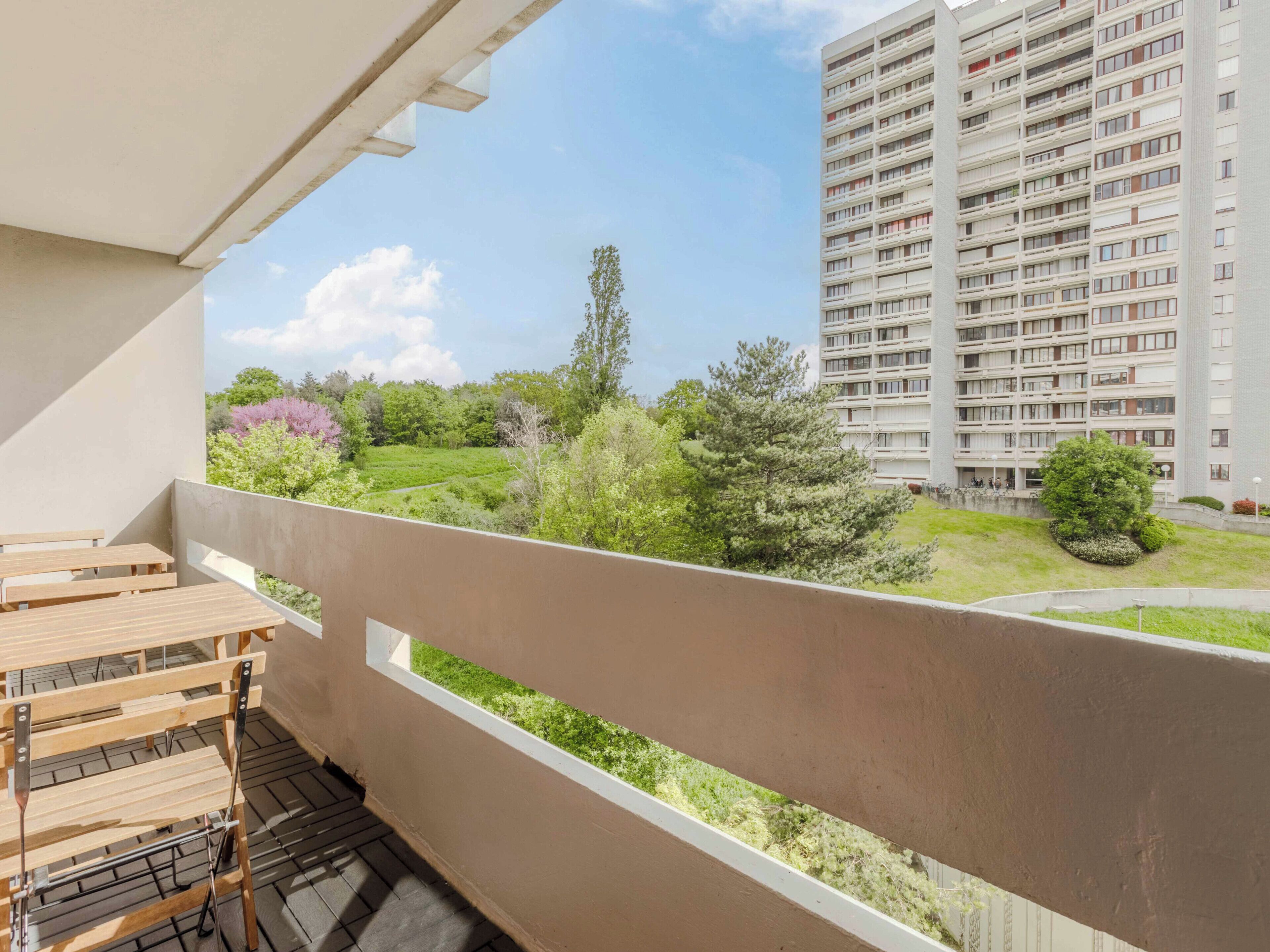 Un balcon donnant sur un parc verdoyant et un grand immeuble d’habitation.