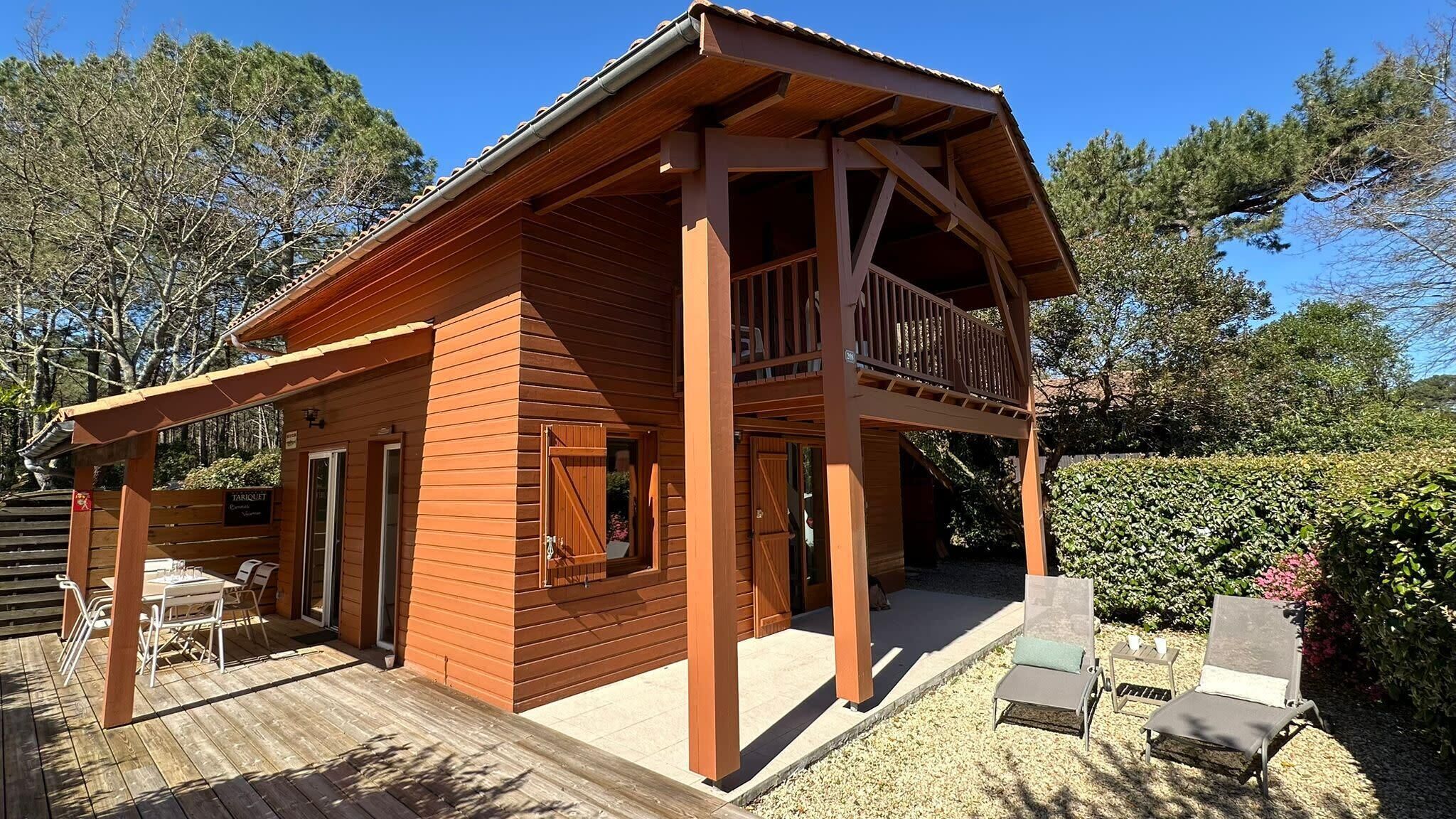Une cabane en bois dotée d’un balcon, d’une terrasse couverte et d’un petit espace extérieur aménagé pour s’asseoir.