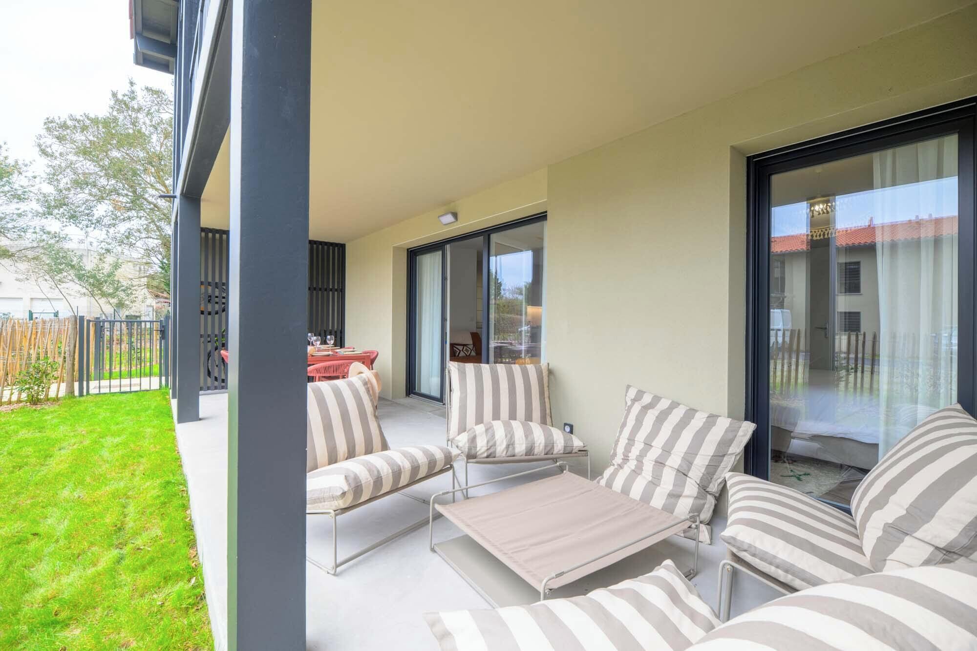 Un'area salotto esterna coperta con cuscini a righe, un tavolo in metallo e una porta vetrata che dà su un patio.