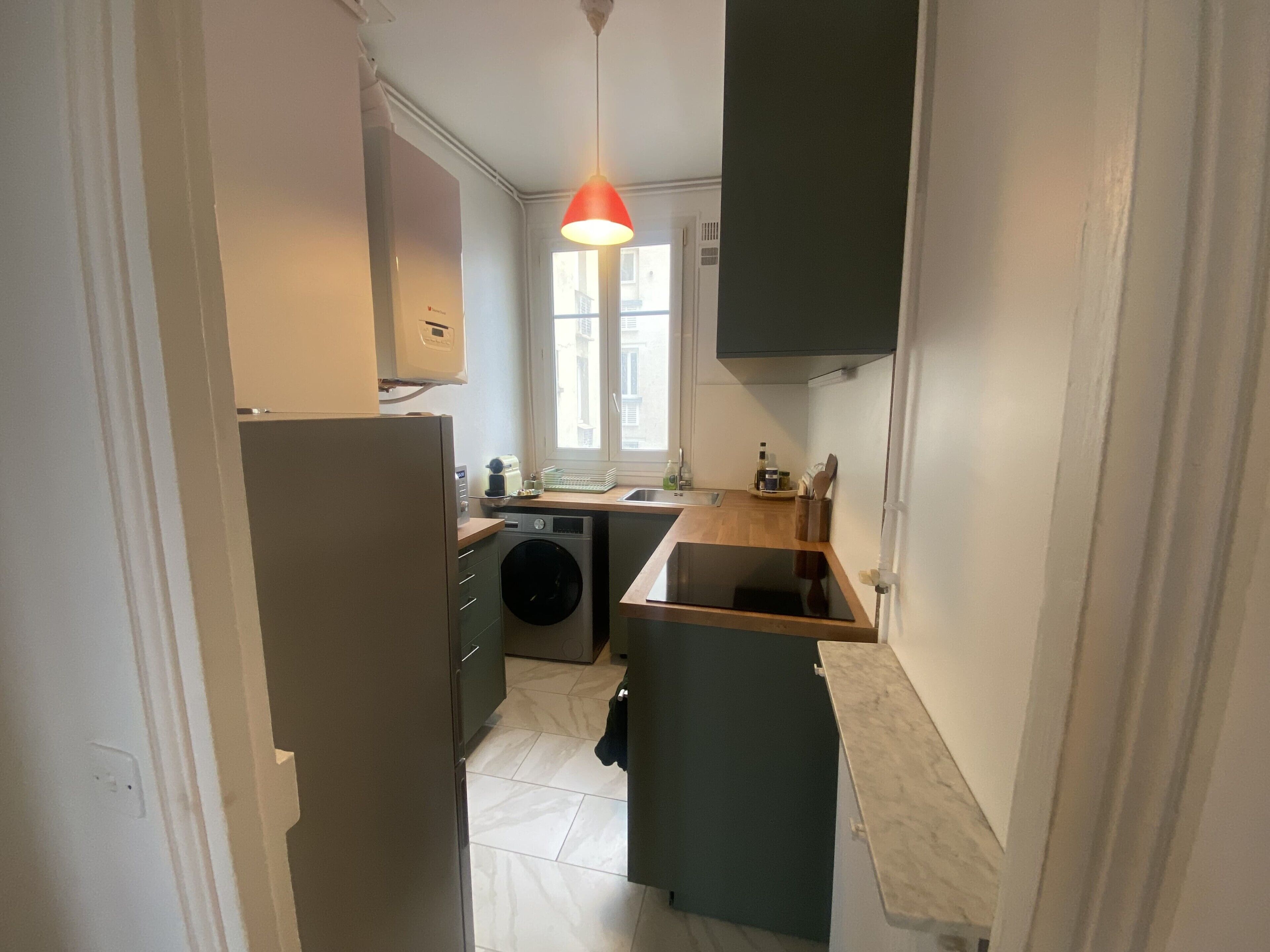 Een kleine keuken met een wasmachine, een spoelbak en een raam.