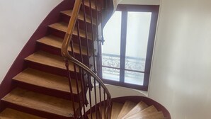 Una scala a chiocciola con gradini in legno e corrimano in metallo, che conduce a una piattaforma con vista sull'esterno.