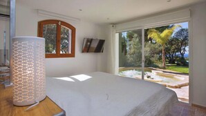 Un dormitorio con cama, televisión, ventana y vistas a un jardín.