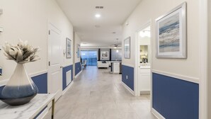 A hallway with a marble vase, framed artwork, and a view into a room with a kitchen area. - Last Minute Disney Getaway! Private Pool, Game Room & Themed Bedrooms. Book Now! #163615 (Orlando)