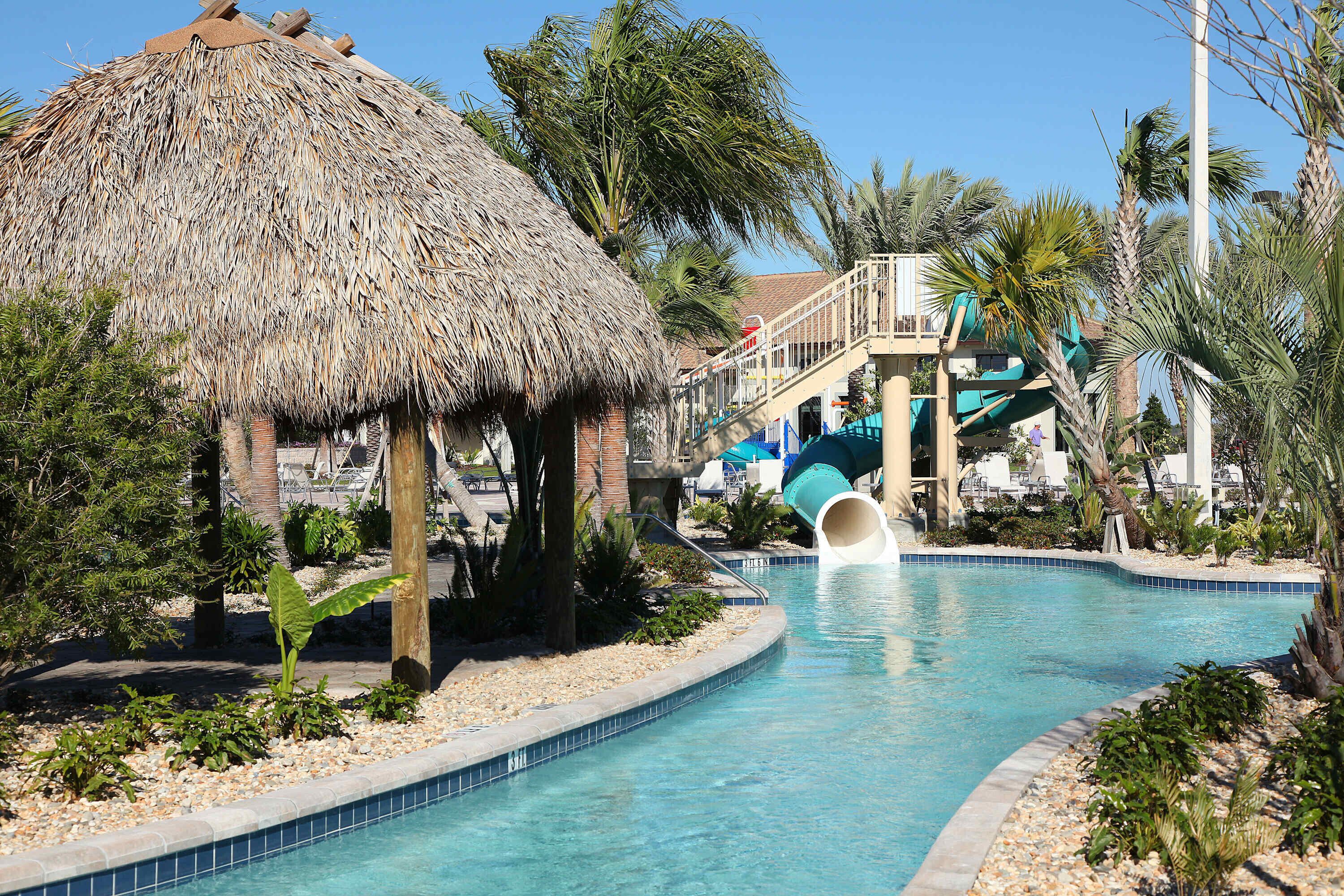 Ein Pool mit Wasserrutsche, einer Struktur mit Reetdach und Palmen.