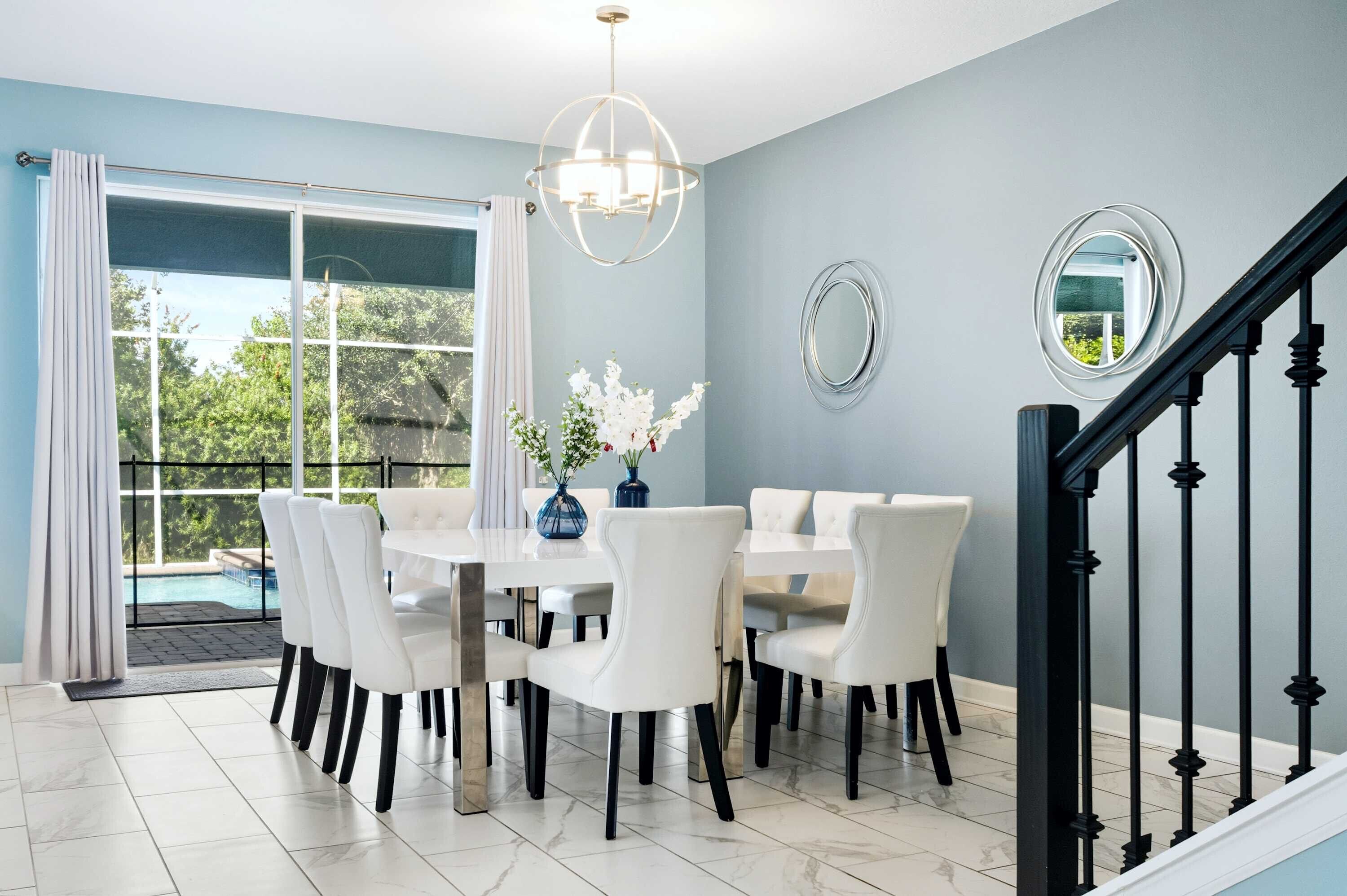 A dining area with a table and chairs, a chandelier, a view of the outdoors, and a staircase.