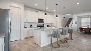 A modern kitchen with white cabinetry, a central island, bar stools, and pendant lighting. - Last Minute Disney Getaway! Private Pool & Themed Bedrooms. Book Now! #163619 (Orlando)