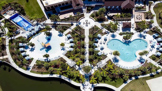 An aerial view of a resort with a central pool, a heart-shaped pool, and surrounding palm trees. - Last Minute Disney Getaway! Private Pool & Themed Bedrooms. Book Now! #163619 (Orlando)