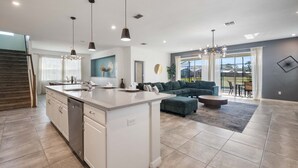 A modern kitchen with a central island, a dining area with a round table, and a living room with a sofa and a large window. - Last Minute Disney Getaway! Private Pool & Themed Bedrooms. Book Now! #163619 (Orlando)