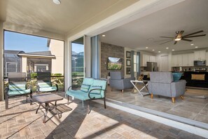 Eine geräumige Terrasse mit Gartenmöbeln, Deckenventilator und einem durchgehenden Gang zur Küche.