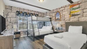Ein Schlafzimmer mit Etagenbett, einem Doppelbett, Steinwänden, einem Fernseher, einem Fenster mit Jalousien und einer Wand mit Bannern der Hogwarts-Häuser.