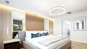 Une chambre à coucher moderne avec un grand lit, des tables de chevet, une télévision et un lustre.