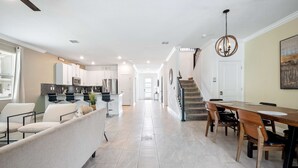 Una cocina moderna con armarios blancos, un comedor con mesa y sillas de madera, y una escalera que sube a otro nivel.
