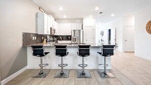 Una cocina moderna con armarios blancos, electrodomésticos de acero inoxidable y una isla central con taburetes de bar.