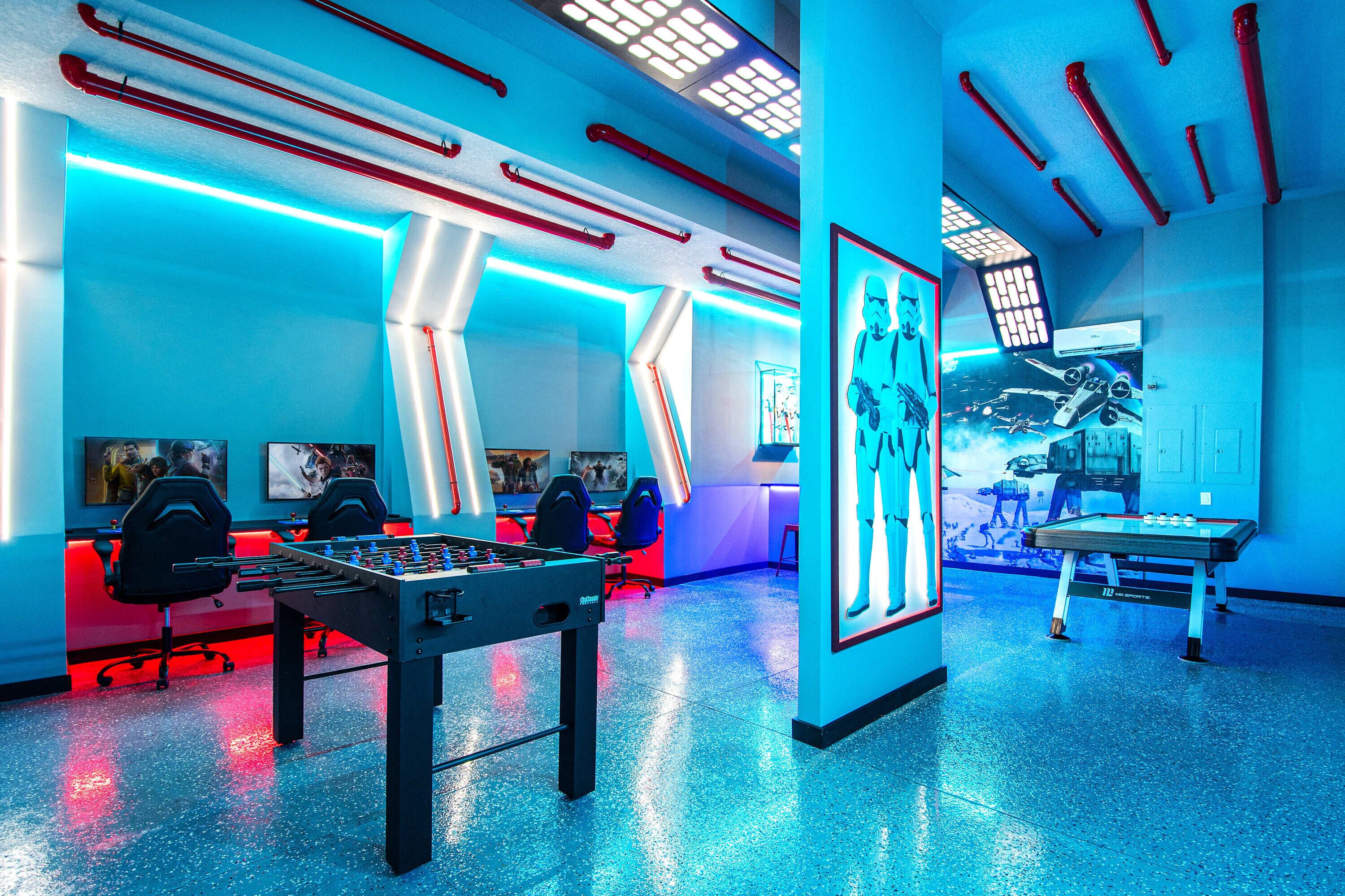 A room with a foosball table, a desk with a computer, and a wall with a Star Wars poster.