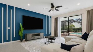 Una sala moderna con un televisor de pantalla plana, un sofá, una mesa de centro y un ventanal con vistas a una piscina.