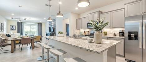A modern kitchen with a large island, stainless steel appliances, and pendant lighting.