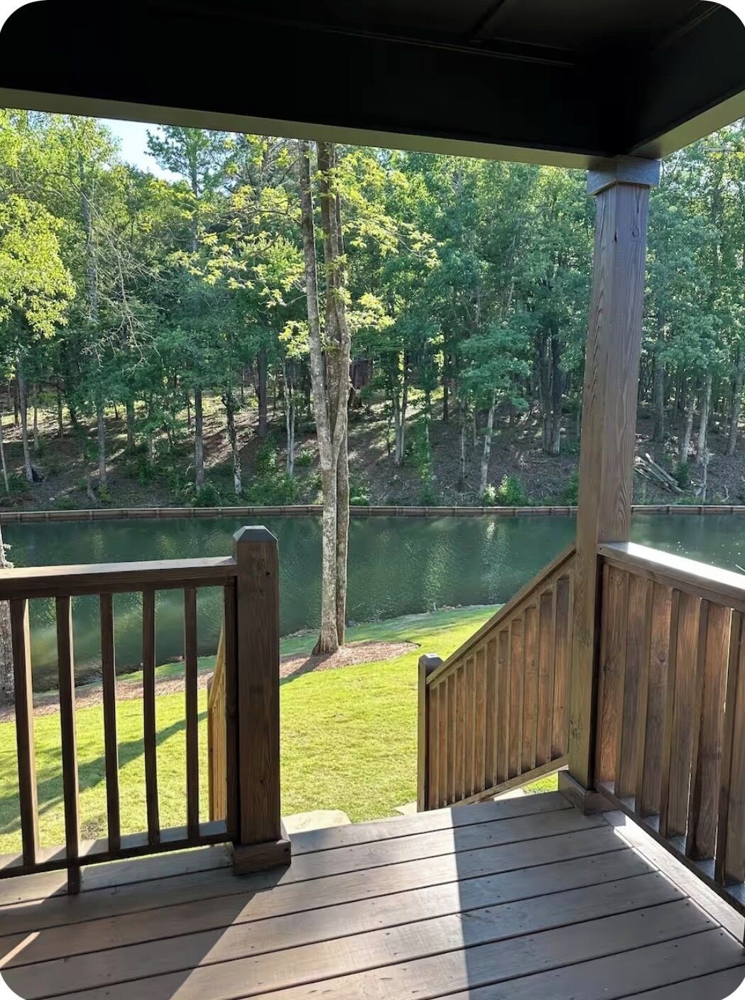 Una terraza de madera con barandilla que da a un lago rodeado de árboles.