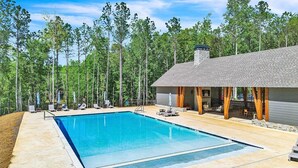 Ein Pool mit Liegestühlen, eine überdachte Terrasse und ein steinernes Gebäude, umgeben von Bäumen.