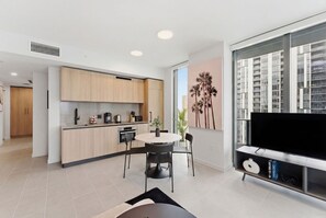 A modern kitchen with wooden cabinets, a dining table with chairs, a TV on a stand, and a large window with a city view. - Miami 169 - One Bedroom Apartment, Sleeps 4 (Miami)