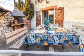Un espacio de comedor al aire libre con una mesa dispuesta para cuatro personas, rodeado de muros de piedra y bancos de madera.