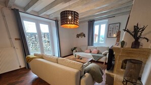 A living room with a sofa, a coffee table, a fireplace, and a hanging light fixture. - Charming “La Ferme du Château” – Private Terrace, Peaceful Setting, Fresh Air (Venon)