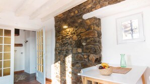 A room with a stone wall, a white door, a table with a basket of fruit, and a green vase. - Charming “La Ferme du Château” – Private Terrace, Peaceful Setting, Fresh Air (Venon)