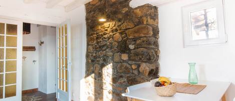 A room with a stone wall, a white door, a table with a basket of fruit, and a green vase.