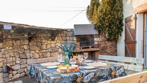 An outdoor dining area with a stone wall, a wooden bench, and a table set for a meal. - Charming “La Ferme du Château” – Private Terrace, Peaceful Setting, Fresh Air (Venon)