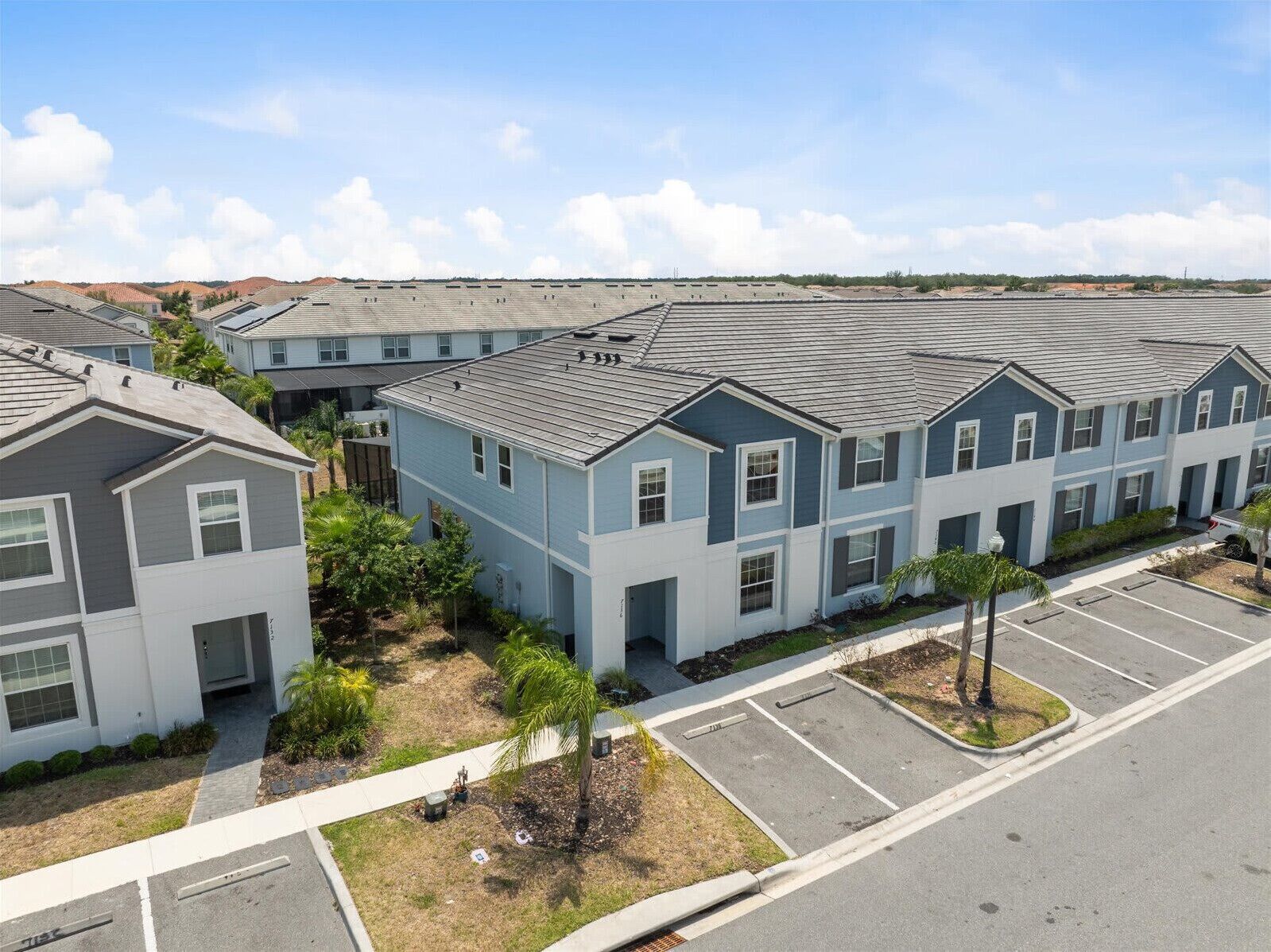 A residential area with multiple two-story houses, a parking lot, and a clear sky.