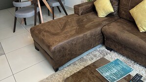 Una sala moderna con un sofá marrón, una mesa de comedor de vidrio, una escalera y una planta verde grande.