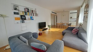 Ein modernes Wohnzimmer mit einer Couch, einem Fernseher, einem Bücherregal und einem Essbereich.