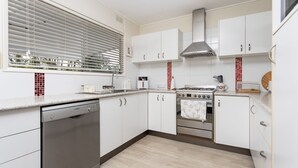 A modern kitchen with white cabinets, a Bosch dishwasher, a stove, and a window with blinds.