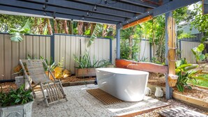A covered outdoor area with a wooden bench, a white hot tub, and various potted plants.