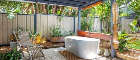 A covered outdoor area with a wooden bench, a white hot tub, and various potted plants.
