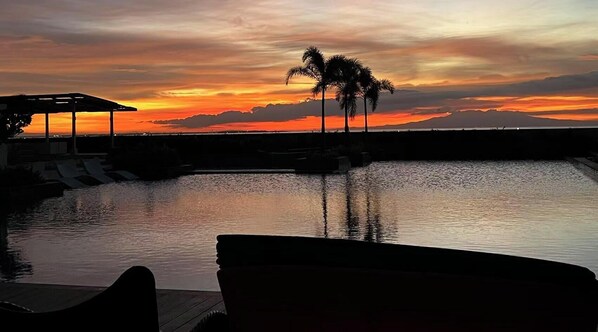 A sunset view over a calm body of water with a pool and lounge chairs. - 3BR with Balcony&Bayview Okada Aiports (Parañaque)