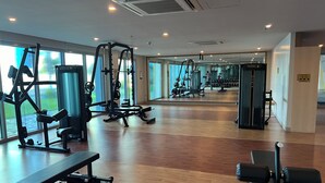Un gimnasio con diversas máquinas de ejercicio, ventanas amplias y suelo de madera.