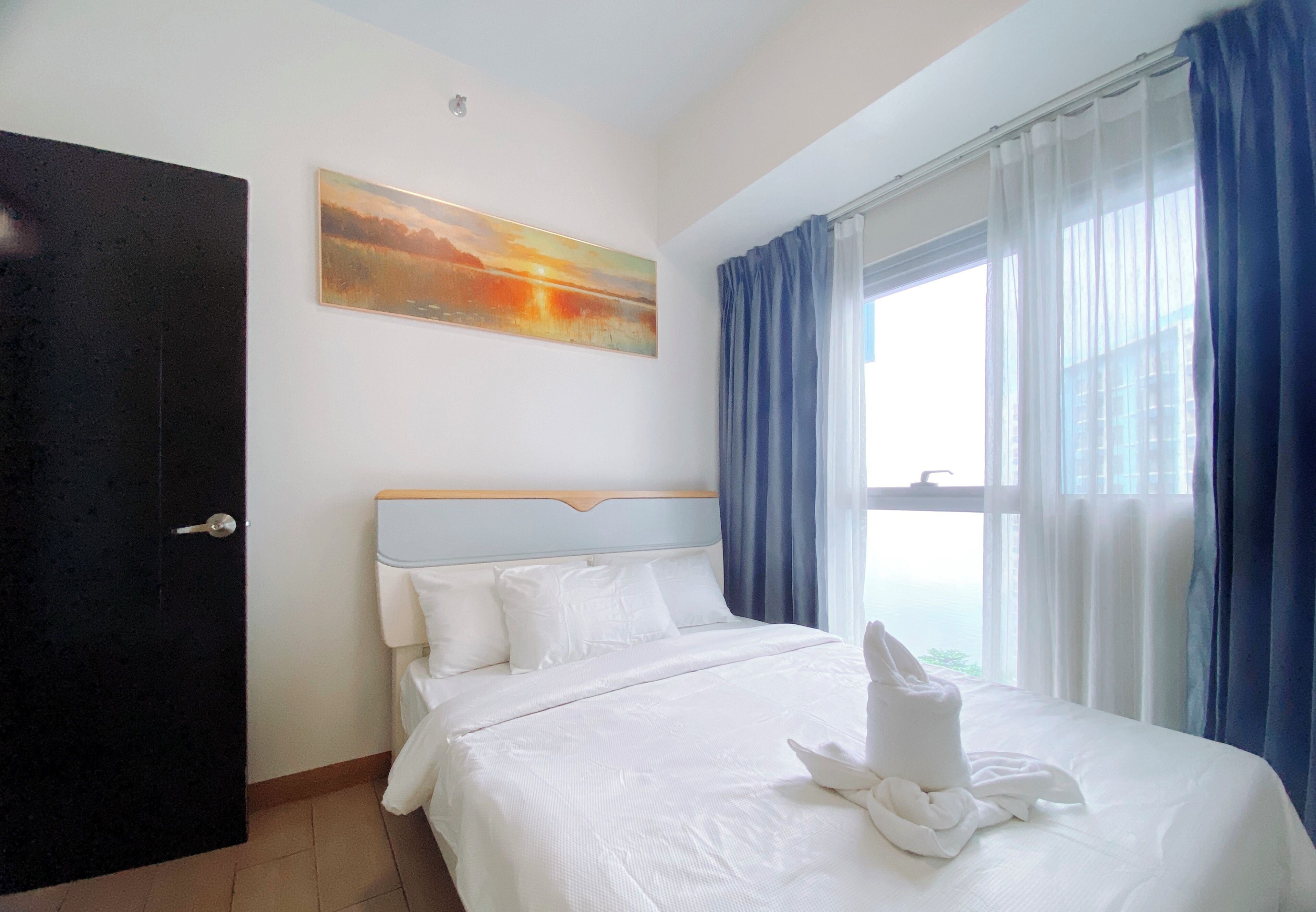 Una camera d'albergo con un letto, un quadro appeso al muro e una finestra con tende.