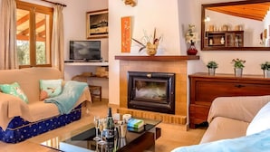 Una sala de estar con sofá, una mesa de centro con bebidas, chimenea, televisor y un mueble de madera.