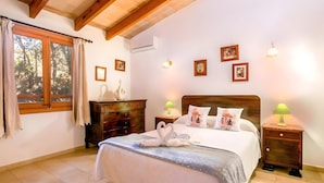 Un dormitorio con cama, mesitas de noche, lámparas de pared, cuadros enmarcados y una ventana con cortinas.