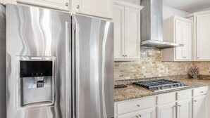 Un refrigerador de acero inoxidable con dispensador de agua, gabinetes blancos, salpicadero de azulejos y estufa a gas.
