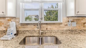 Una cocina con un lavamanos de acero inoxidable, una ventana con vistas a la vegetación y un salpicadero de azulejos.